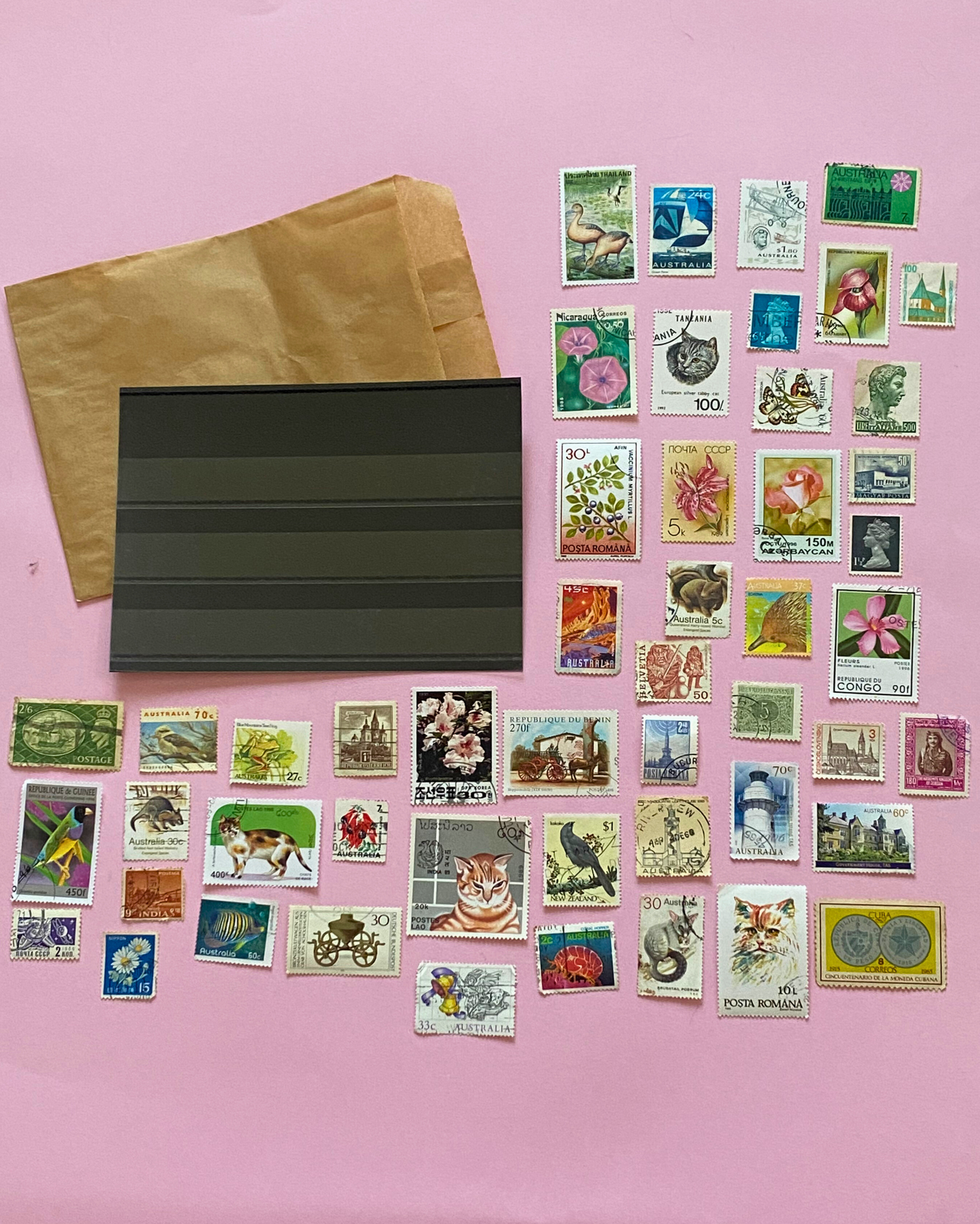 Collection of vintage stamps and a brown envelope on a pink background